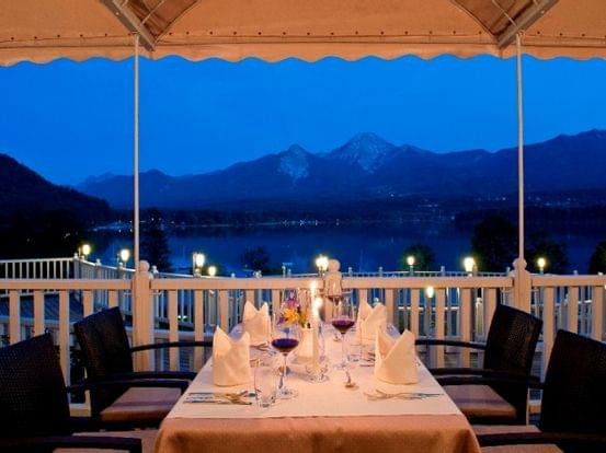 Romantisches Abendessen auf Terrasse mit Blick auf See und Berge bei Dämmerung